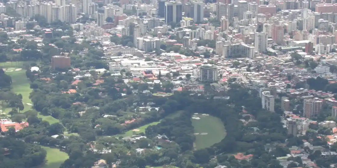 Aerial view of fairways and bunkers among trees and city blocks at Caracas Country Club, Caracas