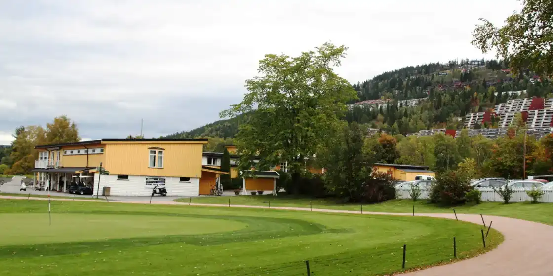 A green beside the clubhouse at Oslo Golfklubb, Bogstad, with wooded hills behind