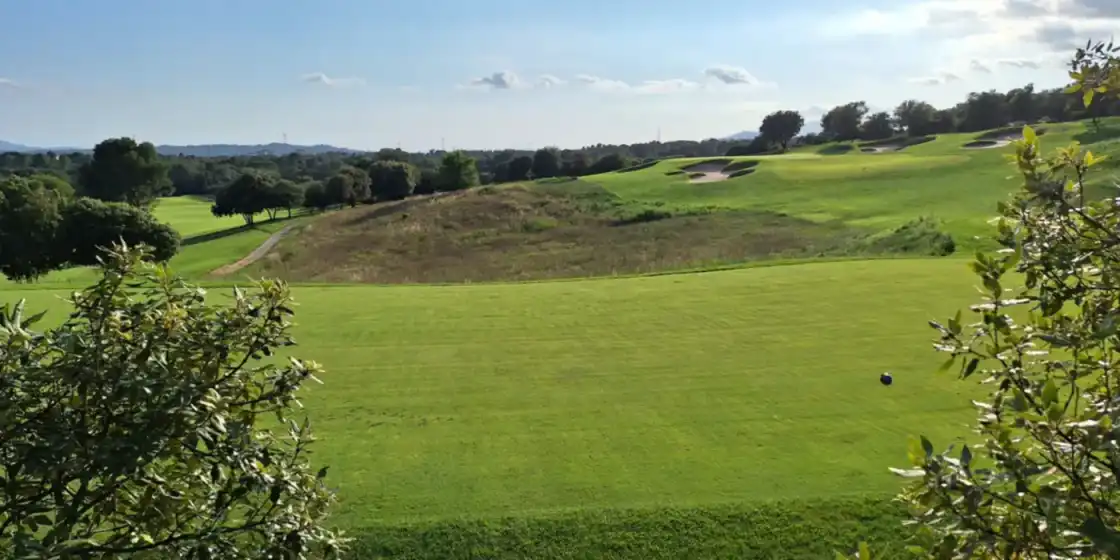 A fairway at Real Club de Golf El Prat in Terrassa, rising toward bunkers and pine