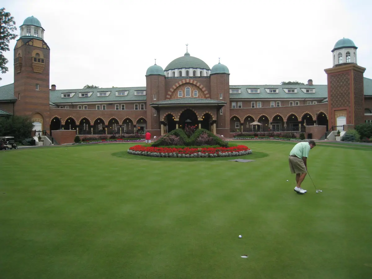 Golfer putting on the practice green in front of the domed Medinah Country Club clubhouse
